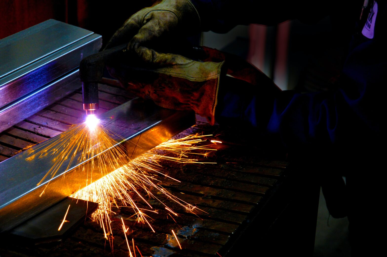 An image of a worker wearing protective clothing using a plasma cutter to cut metal
