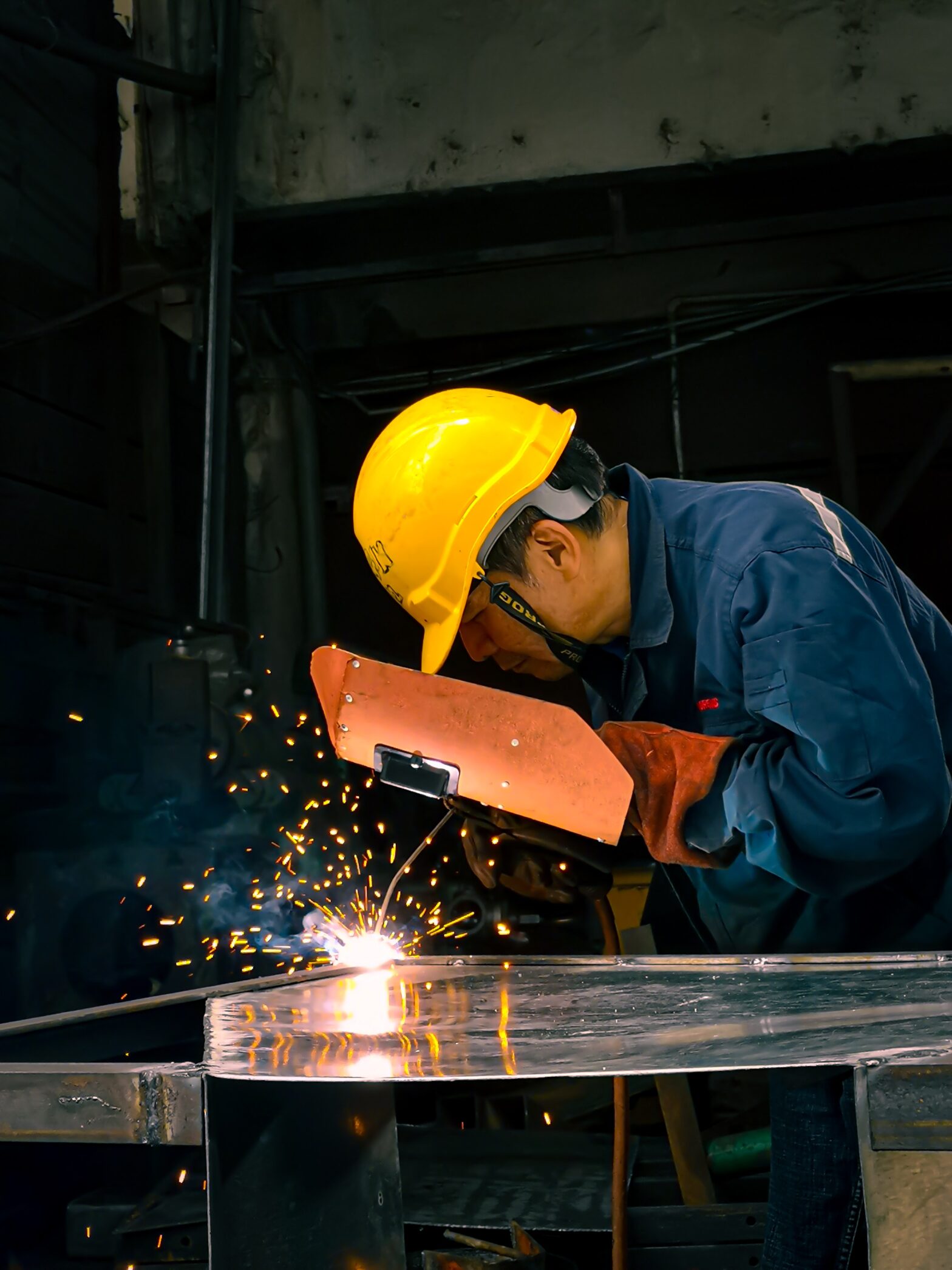 An image of a worker in a yellow hard hat, shielding his face whilst welding